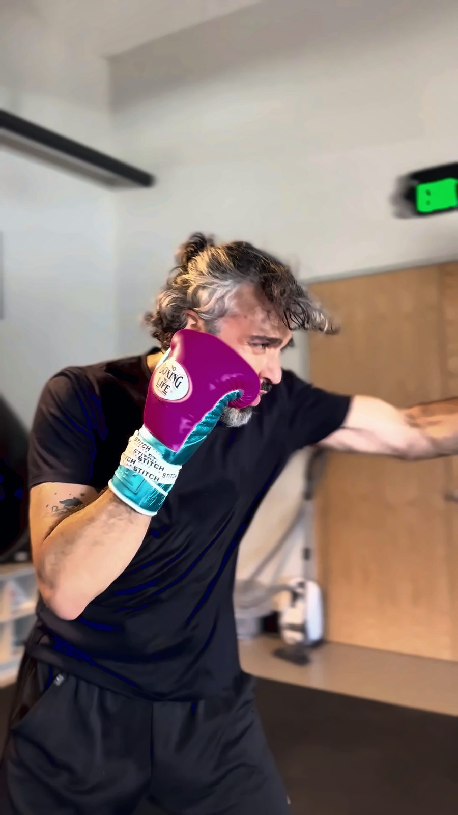 Jaime Camil, in pink gloves, throws a punch at the teal No Boxing No Life heavy bag in the camp gym