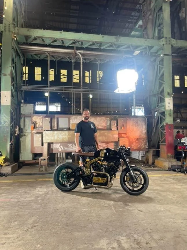 A black-and-gold custom motorcycle and its rider inside a large industrial hall