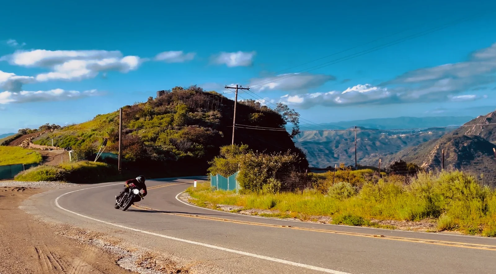 Kris Van Damme riding through a winding canyon road, surrounded by rugged landscapes and open skies.